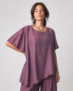 Compleu cu aspect mătăsos, cu top larg și pantalon despicat, în nuanța violet, detaliu al topului.