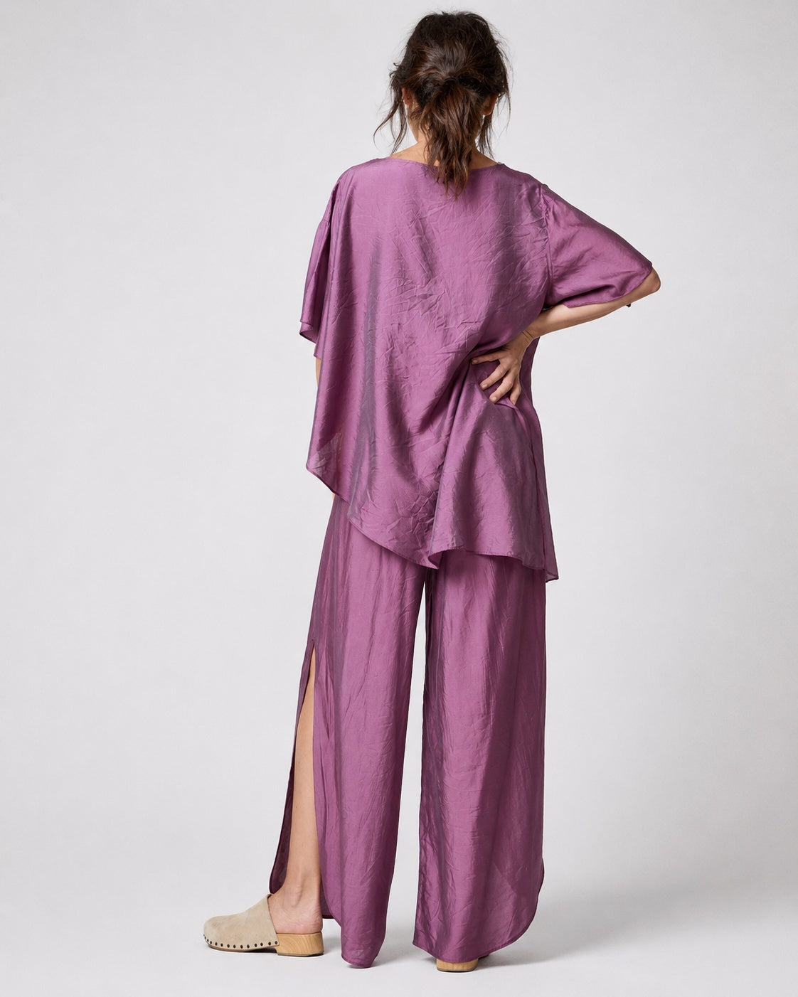 Compleu cu aspect mătăsos, cu top larg și pantalon despicat, în nuanța violet, vedere din spate.