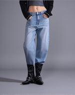 Model poartă blugi barrel fit din denim albastru, cu talie medie și croială lejeră, styling urban, vedere frontală.