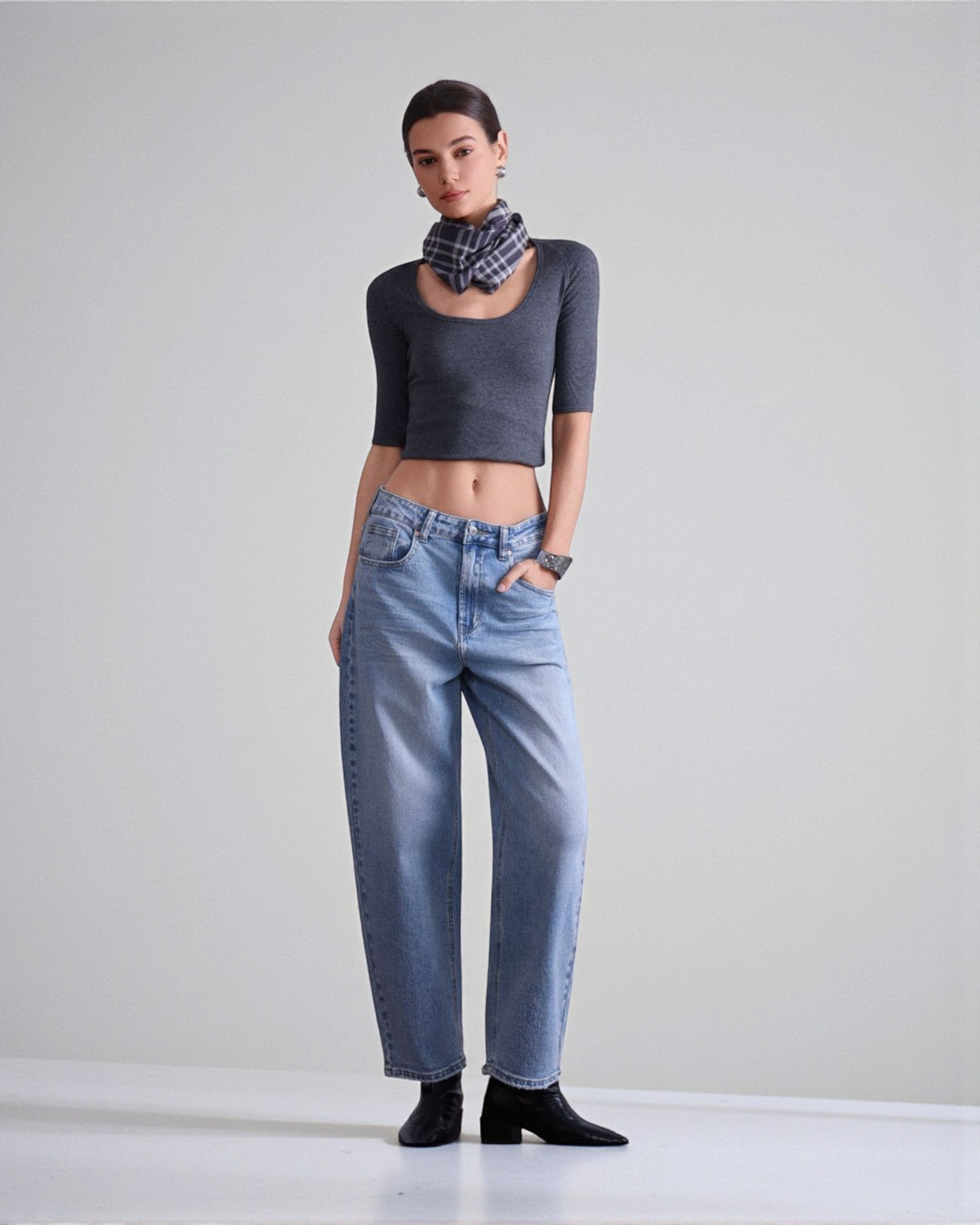 Blugi din denim albastru cu croială barrel fit, purtați cu top scurt și botine, evidențiind linia lejeră a piciorului.