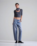 Blugi din denim albastru cu croială barrel fit, purtați cu top scurt și botine, evidențiind linia lejeră a piciorului.