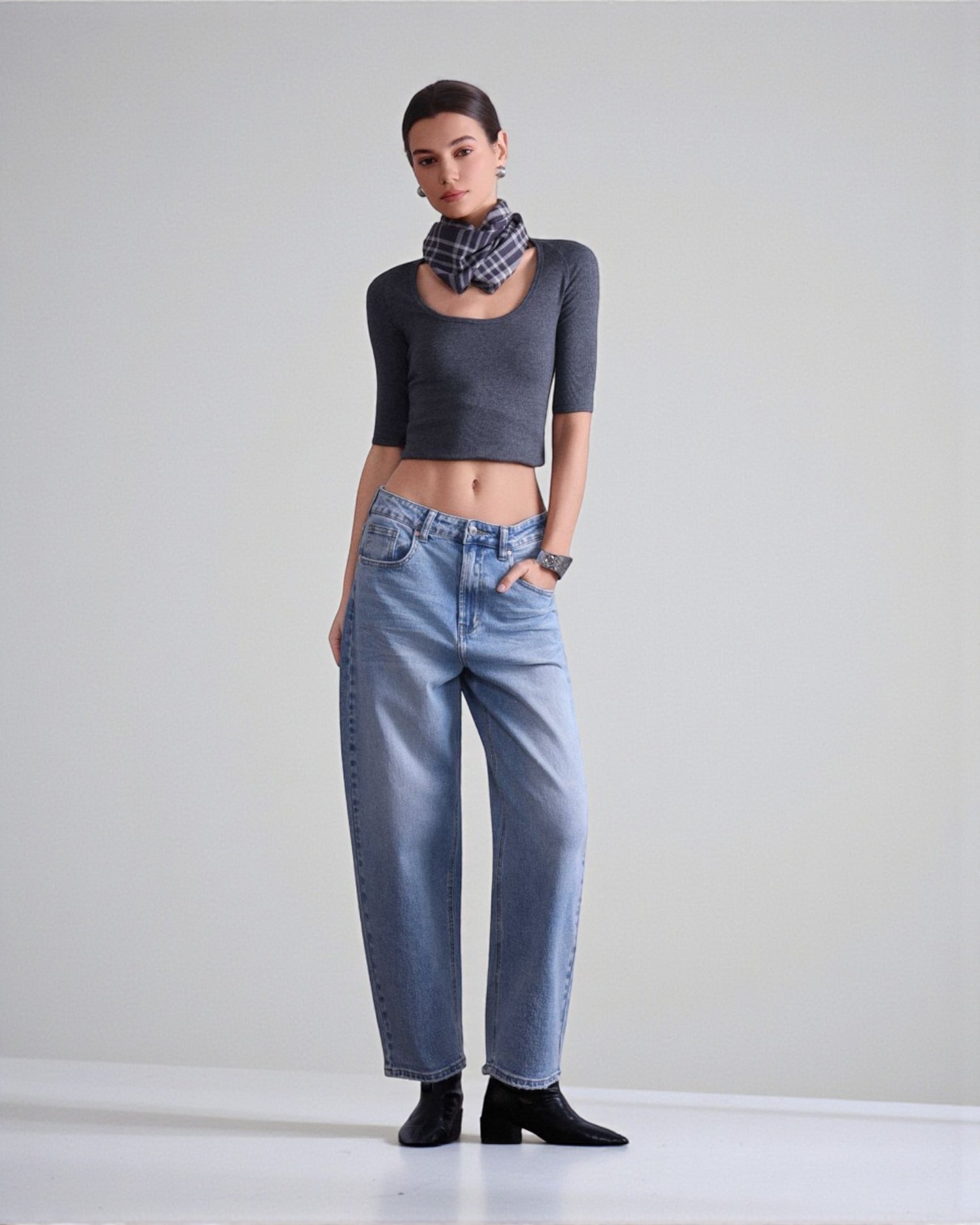 Blugi din denim albastru cu croială barrel fit, purtați cu top scurt și botine, evidențiind linia lejeră a piciorului.