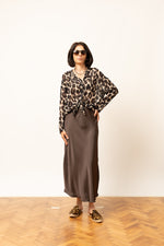 Bluza damă cu imprimeu leopard, purtată cu fustă satinată, mâneci lungi și nod decorativ în talie.