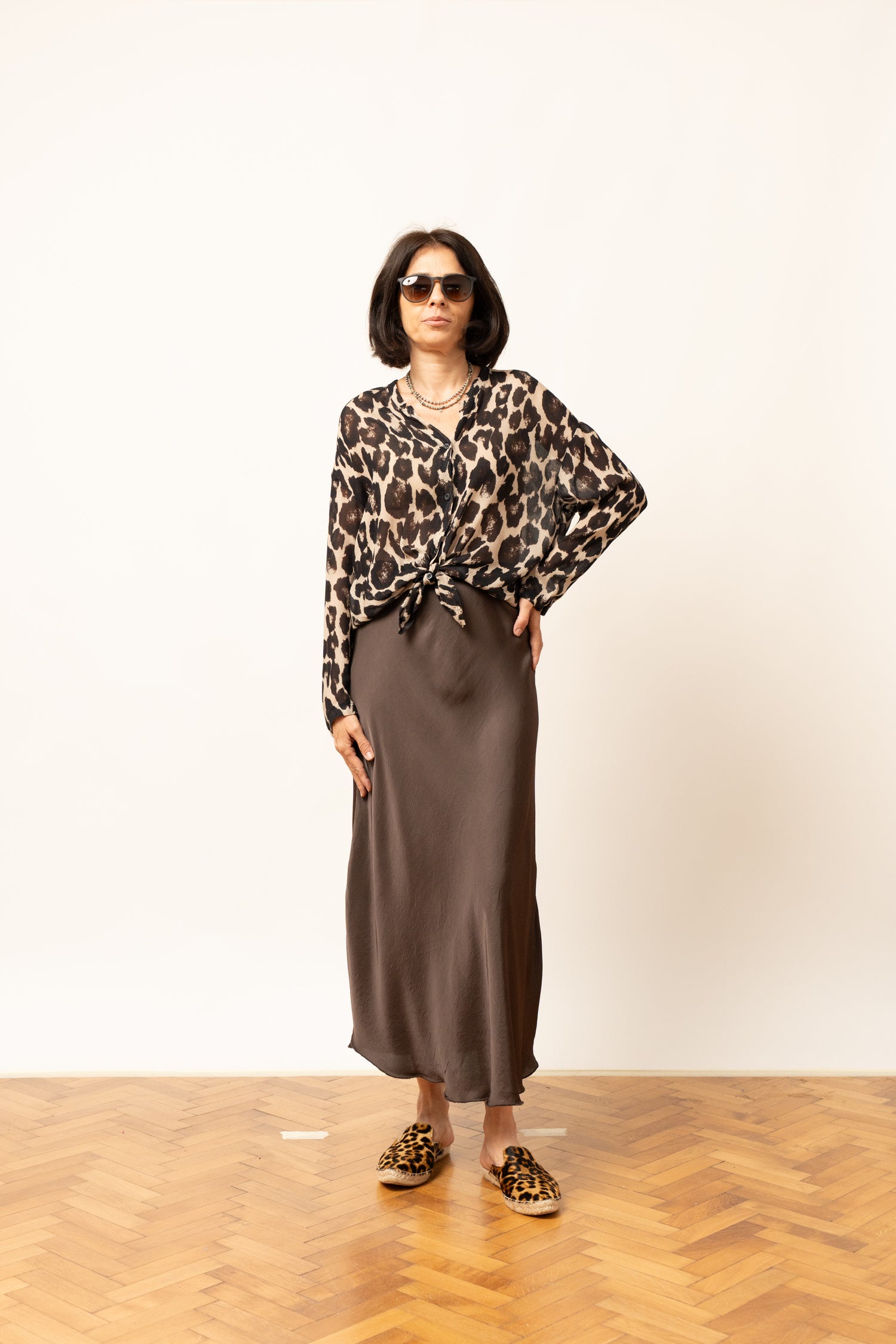 Bluza damă cu imprimeu leopard, purtată cu fustă satinată, mâneci lungi și nod decorativ în talie.