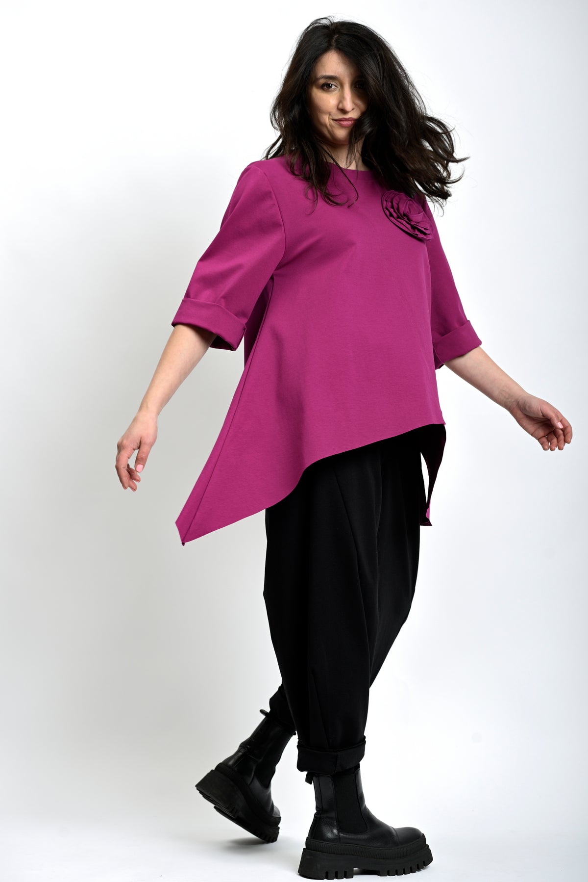 Bluză asimetrică fucsia purtată lateral, evidențiind linia fluidă și mânecile rulate.