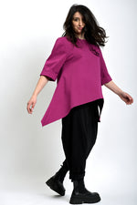 Bluză asimetrică fucsia purtată lateral, evidențiind linia fluidă și mânecile rulate.