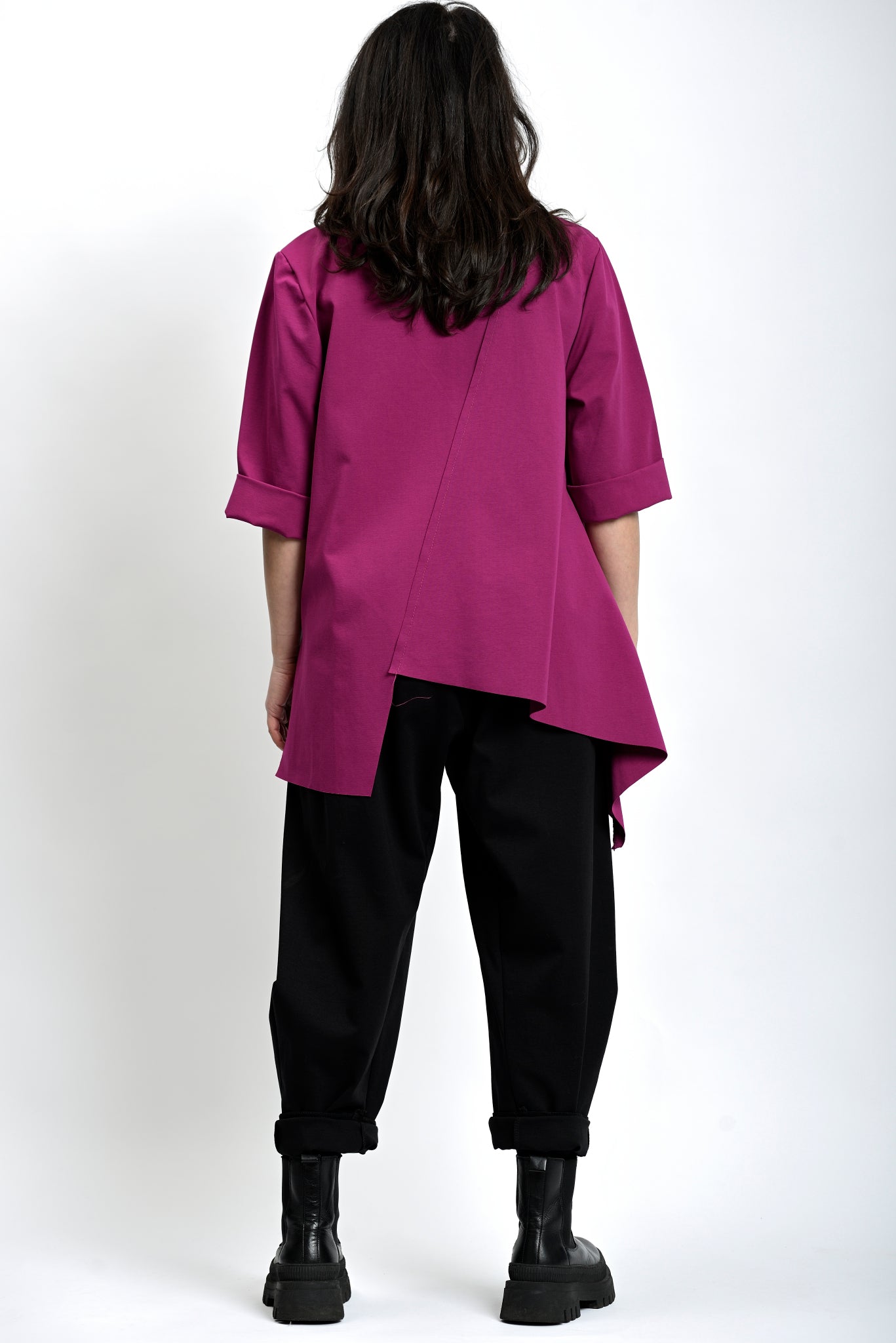 Vedere din spate a bluzei asimetrice fucsia, cu croială lejeră și tiv mai lung.