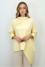 Bluză asimetrică oversize galben pastel, cu colț alungit și umeri căzuți, purtată cu pantaloni bej.