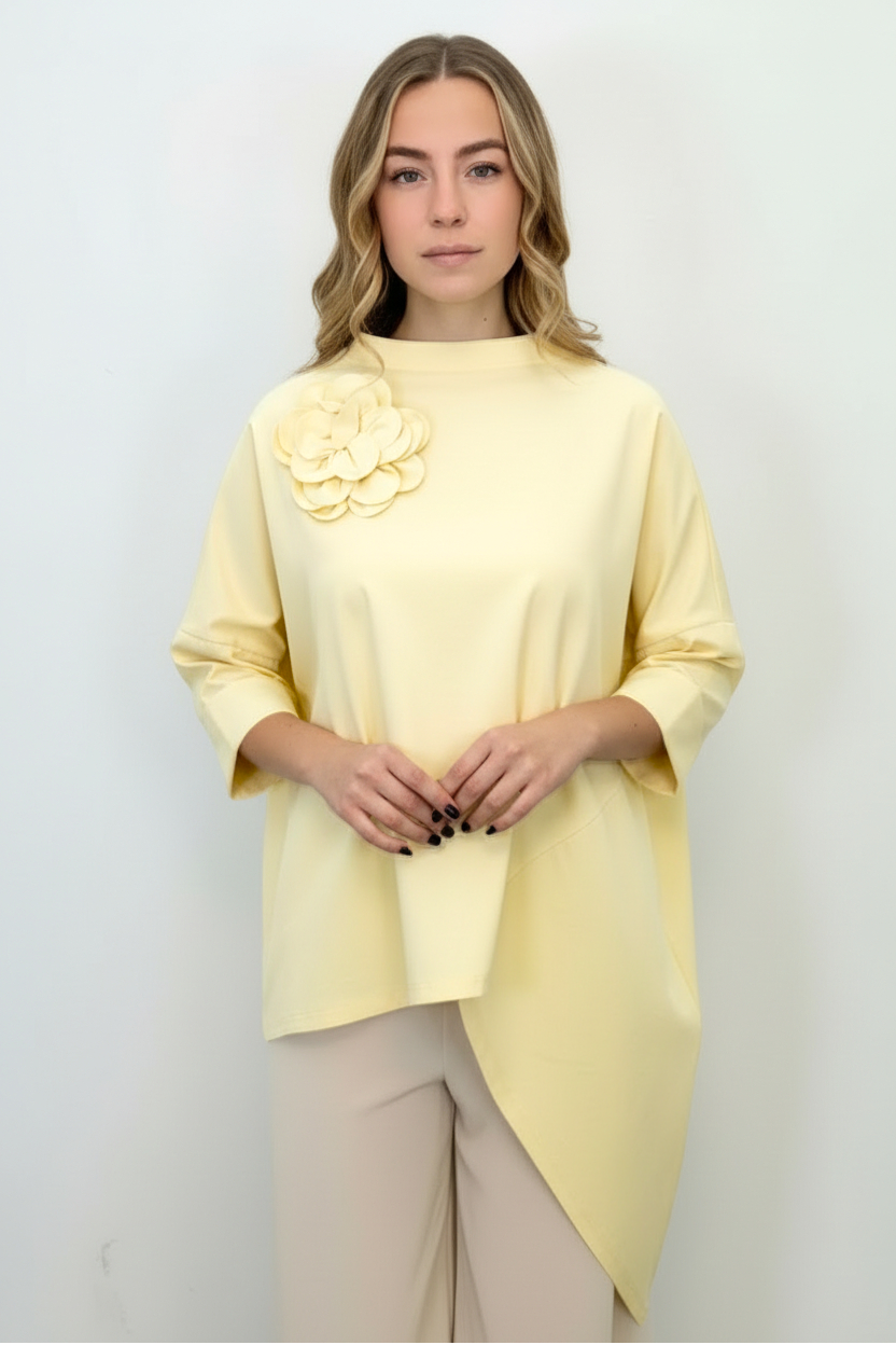 Bluză asimetrică oversize galben pastel, cu colț alungit și umeri căzuți, purtată cu pantaloni bej.