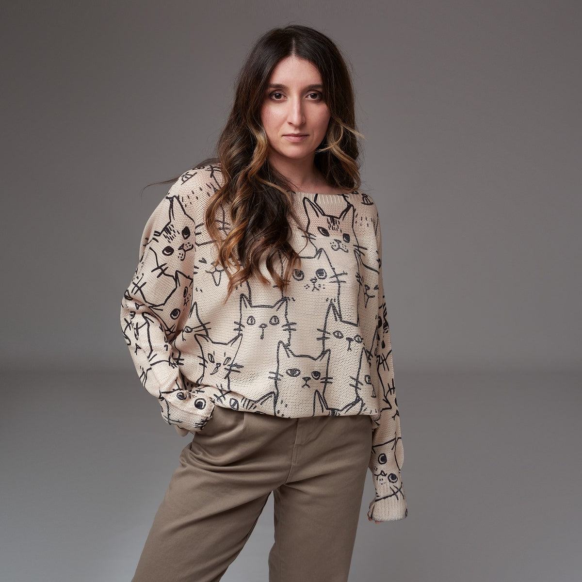 Model purtând bluză bej cu mâneci lungi și imprimeu cu pisici negre, asortată cu pantaloni casual în nuanță neutră.