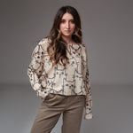 Model purtând bluză bej cu mâneci lungi și imprimeu cu pisici negre, asortată cu pantaloni casual în nuanță neutră.
