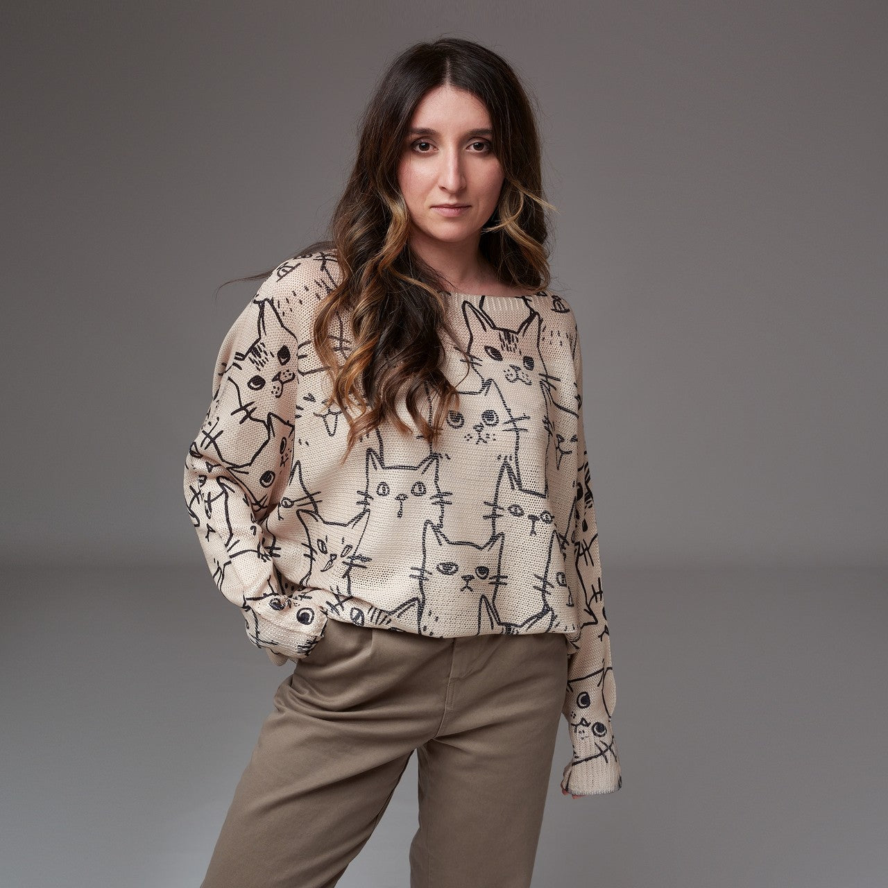 Model purtând bluză bej cu mâneci lungi și imprimeu cu pisici negre, asortată cu pantaloni casual în nuanță neutră.