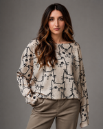 Model purtând bluză bej cu mâneci lungi și imprimeu cu pisici negre, asortată cu pantaloni casual în nuanță neutră.