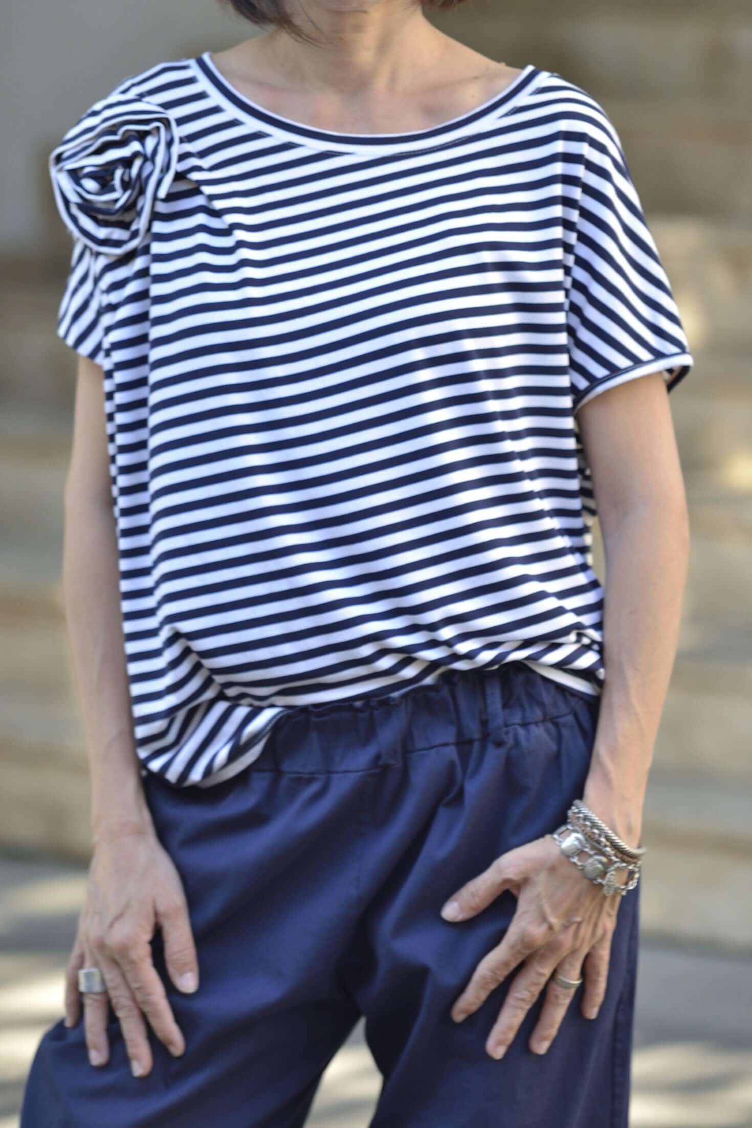 Bluza cu dungi purtată lejer pe umeri, cu floare decorativă în față.