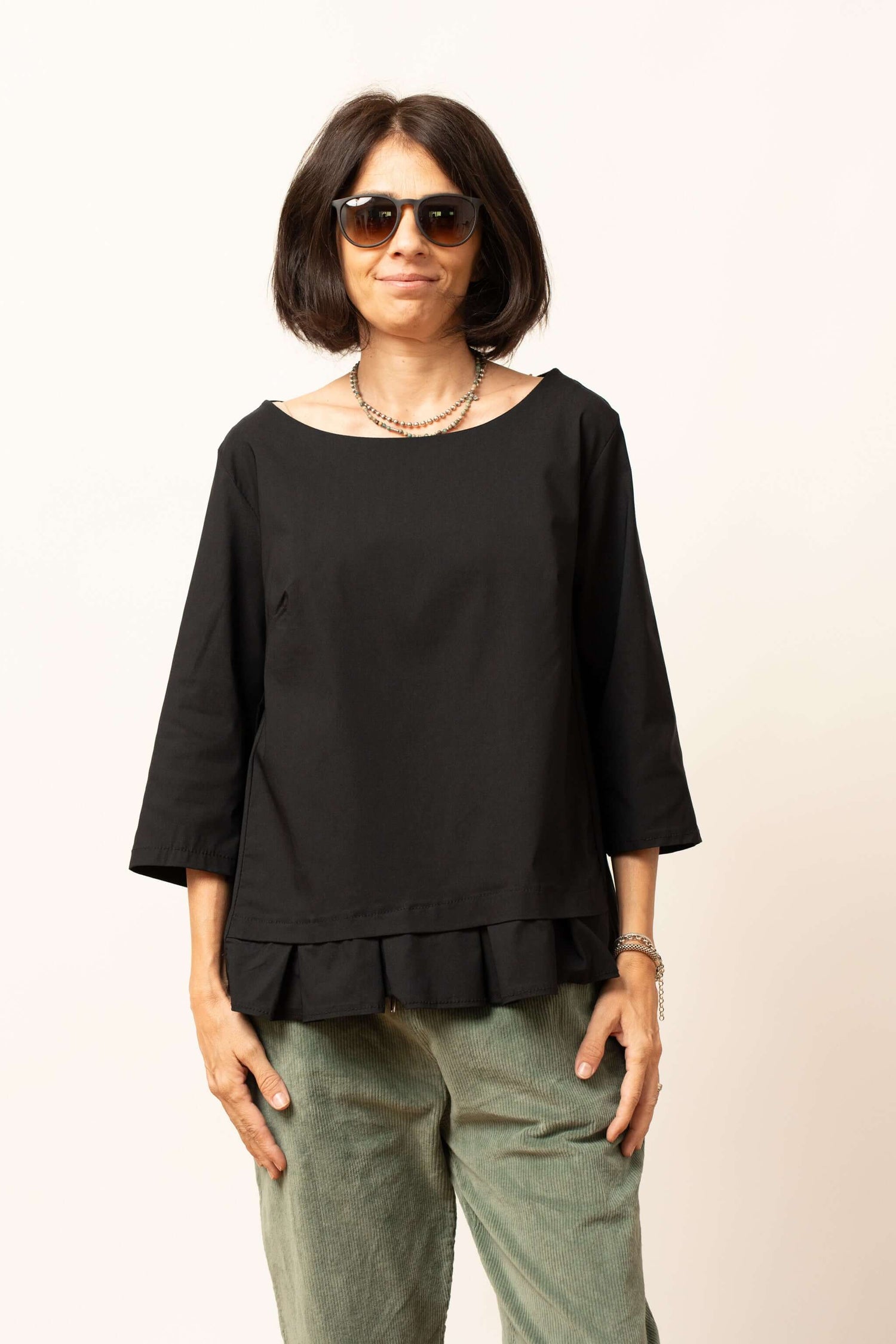 Bluza damă neagră văzută din lateral, cu croială lejeră și volănaș la tiv.