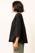 Bluza damă neagră văzută din lateral, cu croială lejeră și volănaș la tiv.