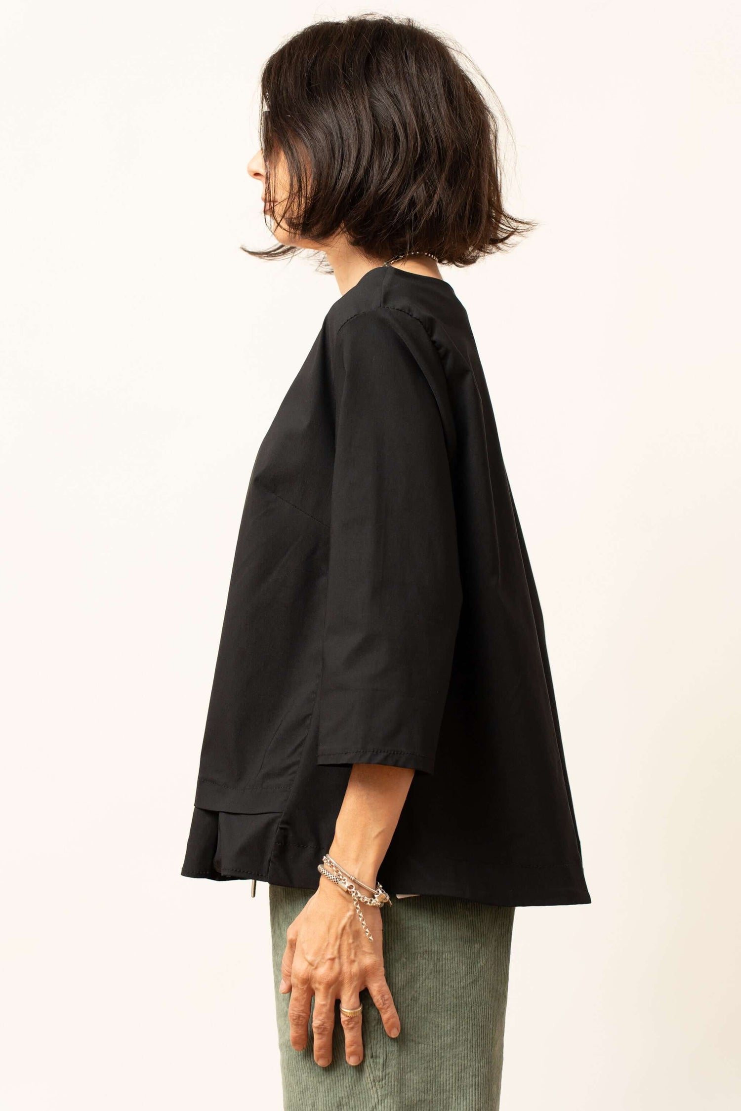 Bluza damă neagră văzută din lateral, cu croială lejeră și volănaș la tiv.