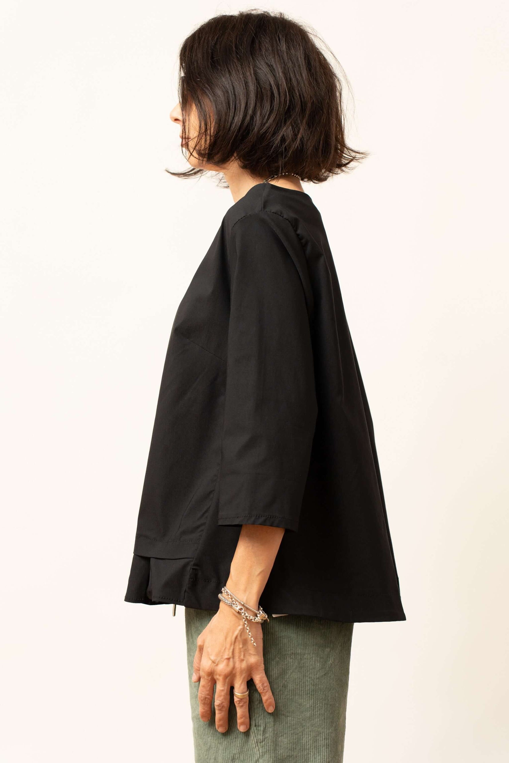 Bluza damă neagră văzută din lateral, cu croială lejeră și volănaș la tiv.