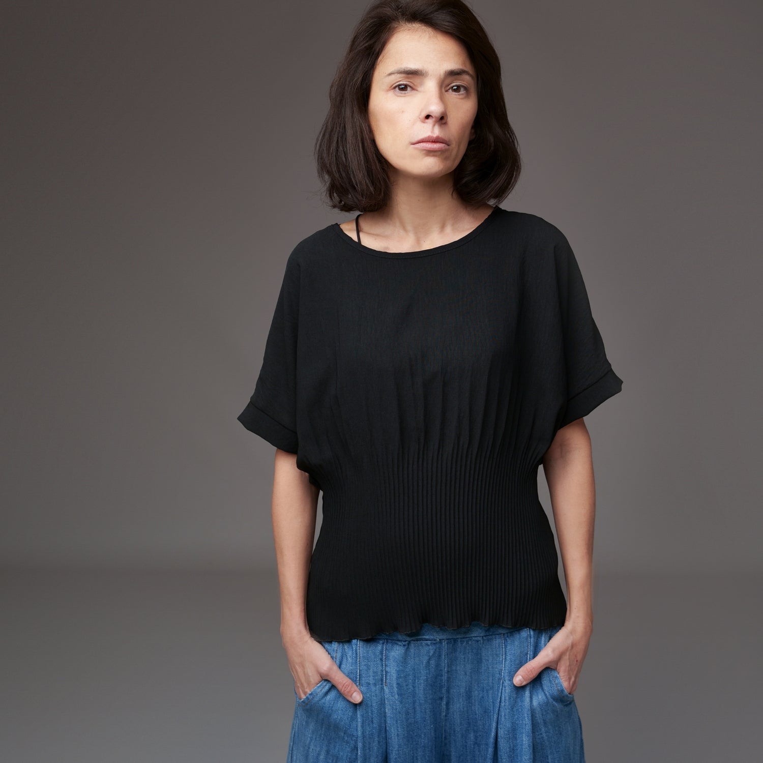 Model purtând bluză neagră cu mânecă scurtă tip fluture, combinată cu pantaloni din denim lejer.