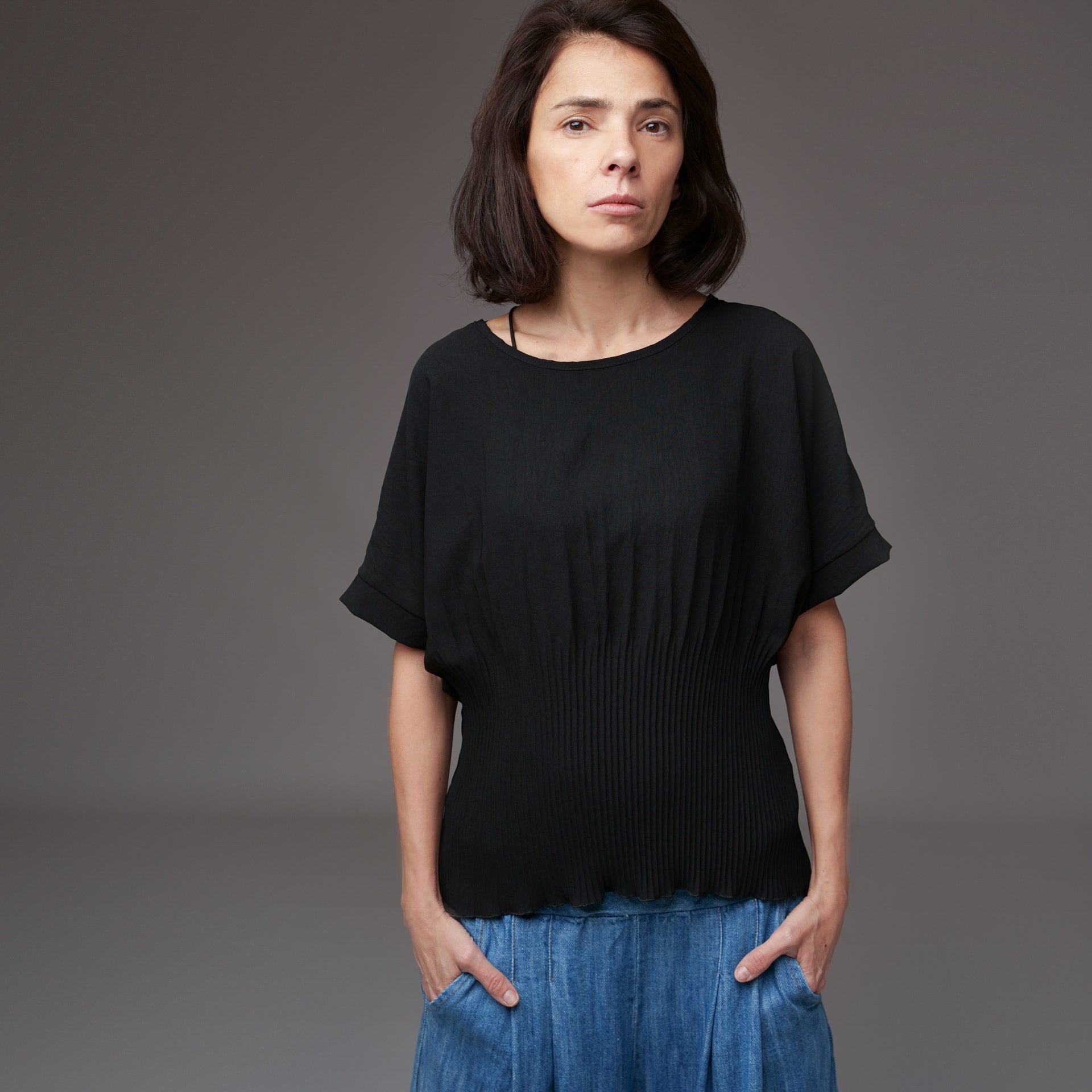 Model purtând bluză neagră cu mânecă scurtă tip fluture, combinată cu pantaloni din denim lejer.