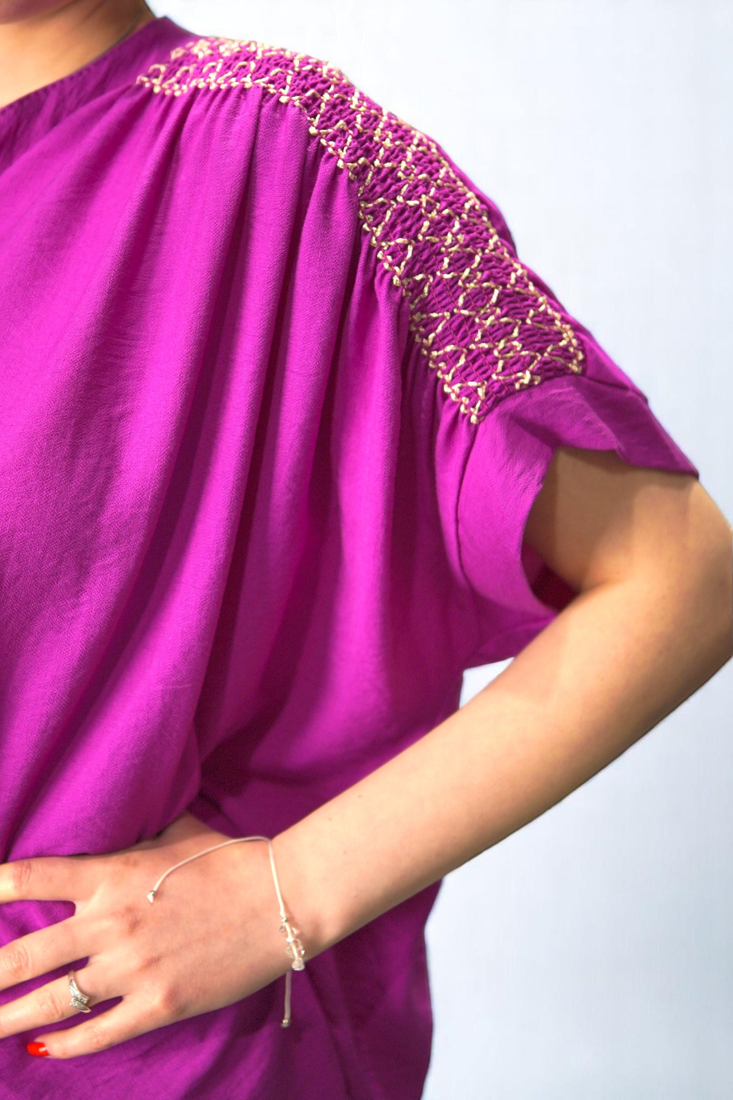 Detaliu broderie decorativă cu fir auriu pe umărul bluzei fucsia, în prim-plan