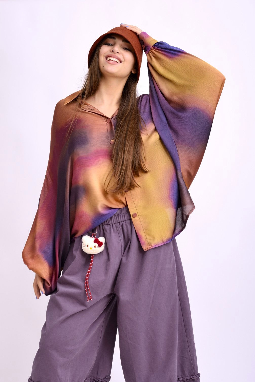 Bluza tip kaftan din material ușor, cu imprimeu gradient în nuanțe de violet, oranj și galben, purtată lejer peste pantaloni.
