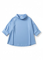 Bluză cu mâneci trei sferturi și guler larg, surprinsă pe fundal neutru, accent pe linia fluidă.