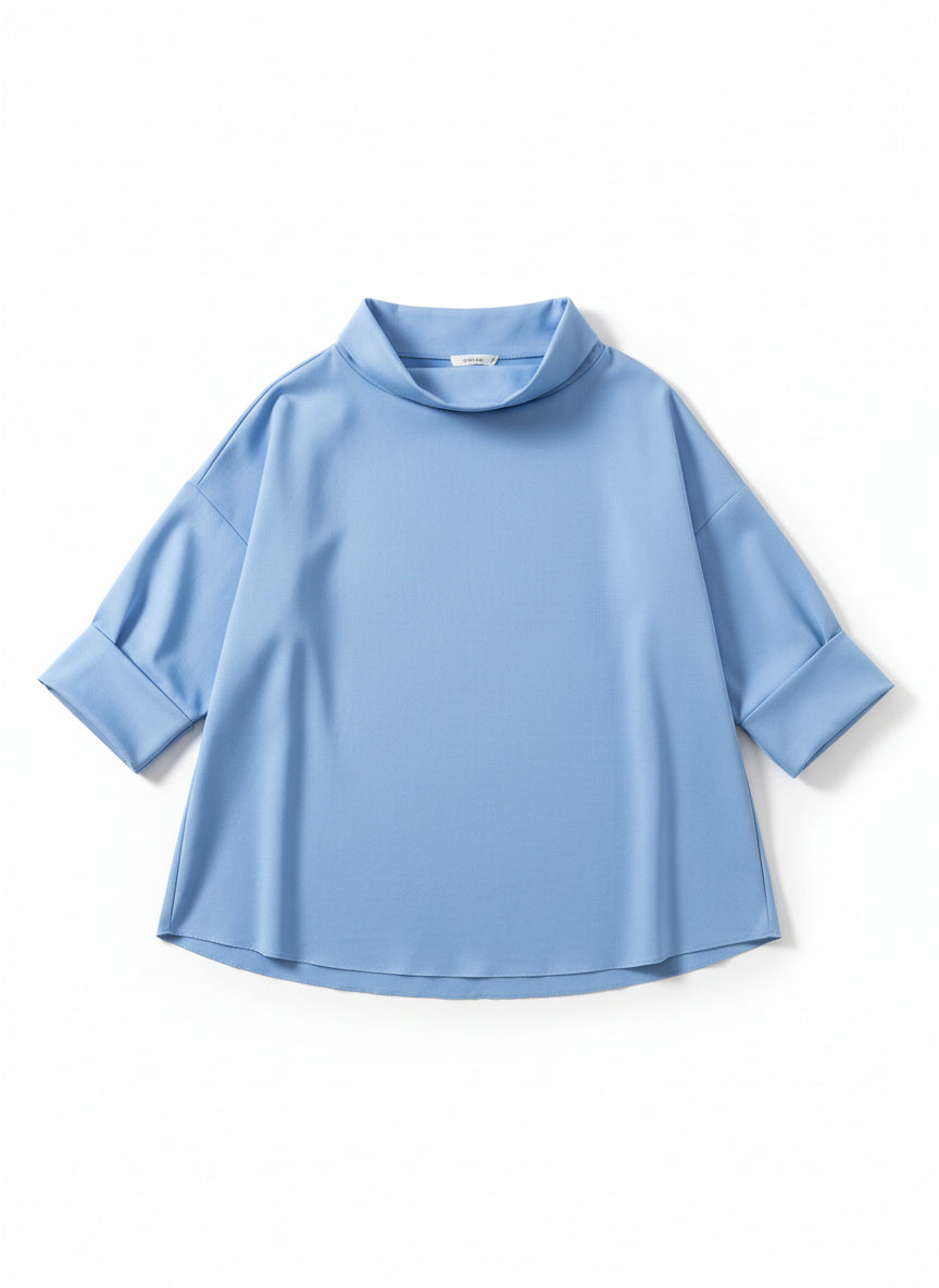 Bluză cu mâneci trei sferturi și guler larg, surprinsă pe fundal neutru, accent pe linia fluidă.