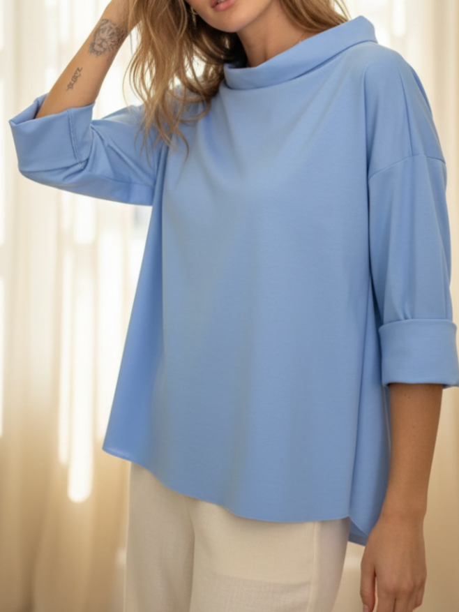 Bluză albastru deschis cu guler amplu și croială lejeră, purtată cu pantaloni deschiși la culoare.