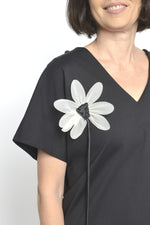 Detaliu frontal al unei bluze negre cu floare decorativă albă aplicată pe umăr.