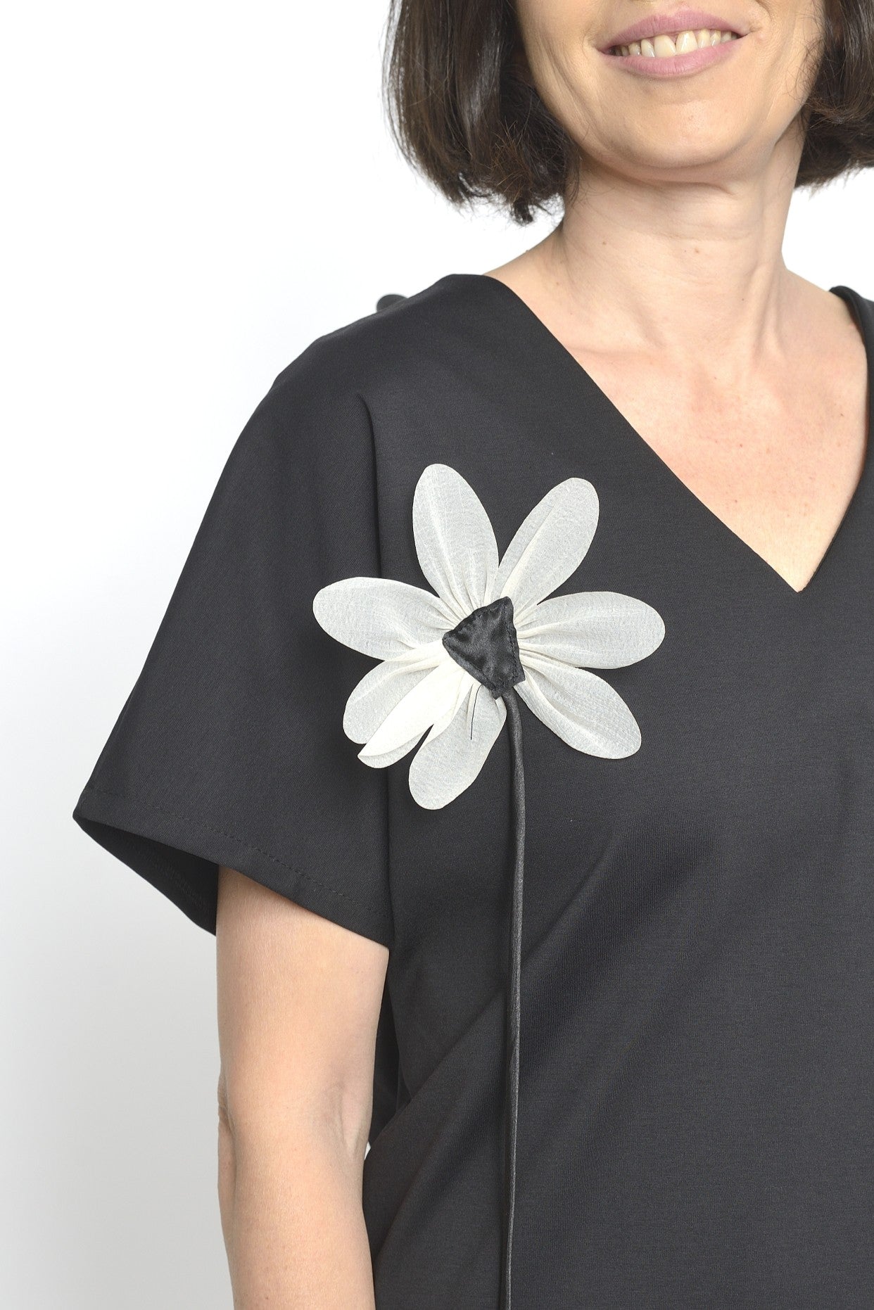 Detaliu frontal al unei bluze negre cu floare decorativă albă aplicată pe umăr.