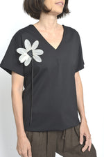 Bluza lungă neagră cu decolteu în V și floare albă decorativă aplicată pe umăr.