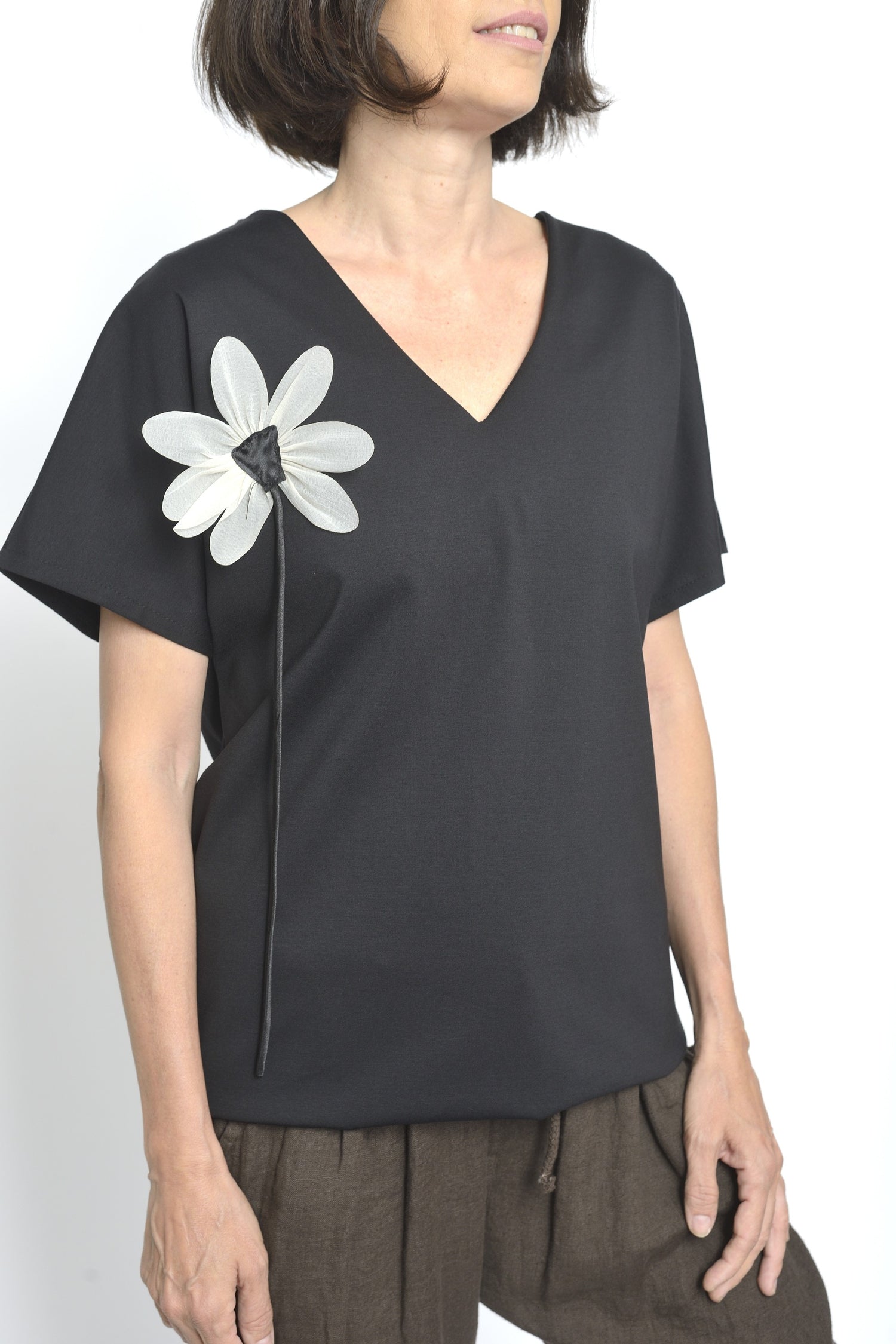 Bluza lungă neagră cu decolteu în V și floare albă decorativă aplicată pe umăr.