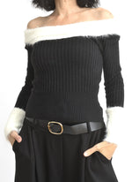 Bluză neagră din tricot cu decolteu pe umeri și bandă pufoasă albă în partea superioară.