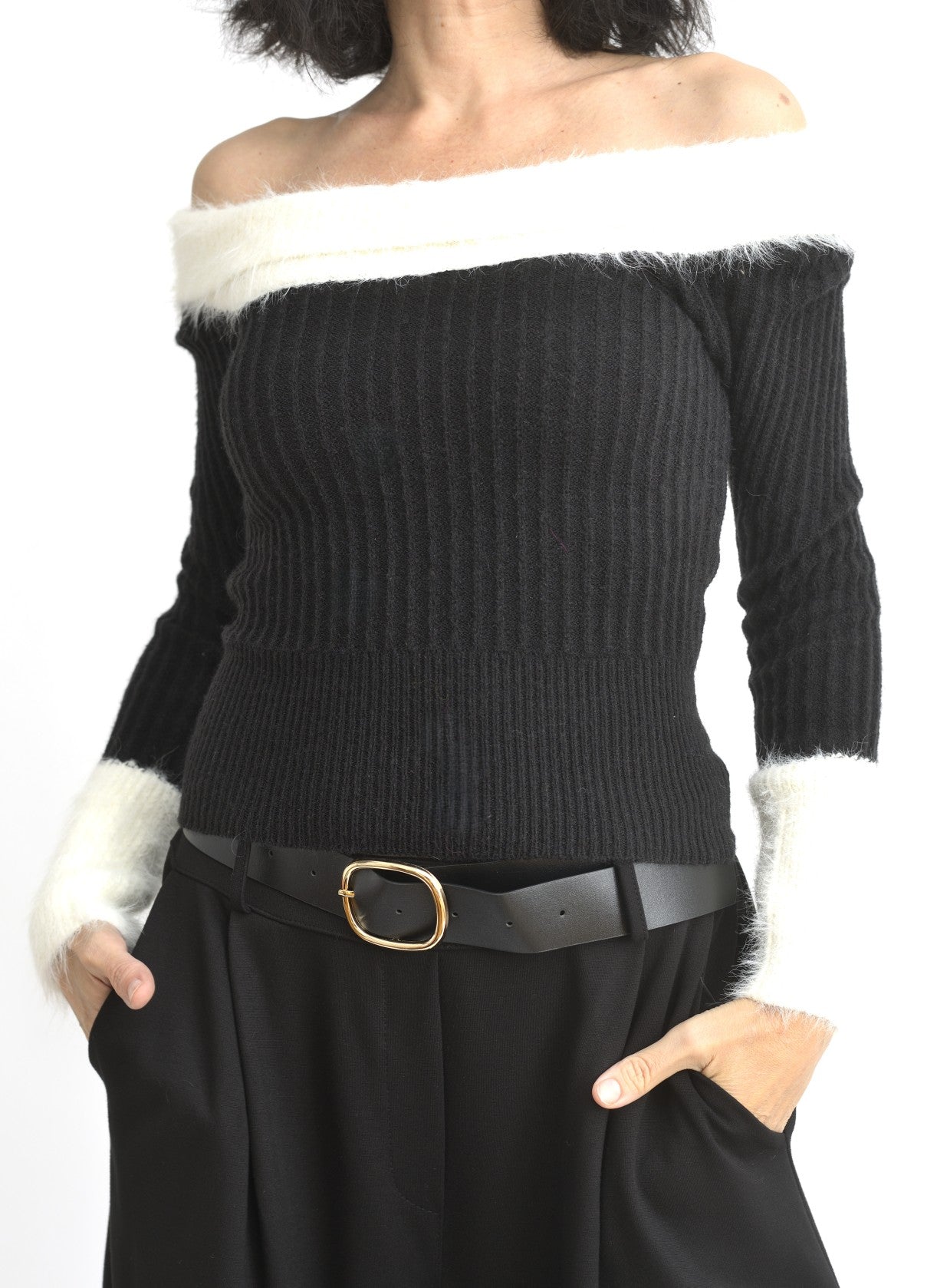 Bluză neagră din tricot cu decolteu pe umeri și bandă pufoasă albă în partea superioară.