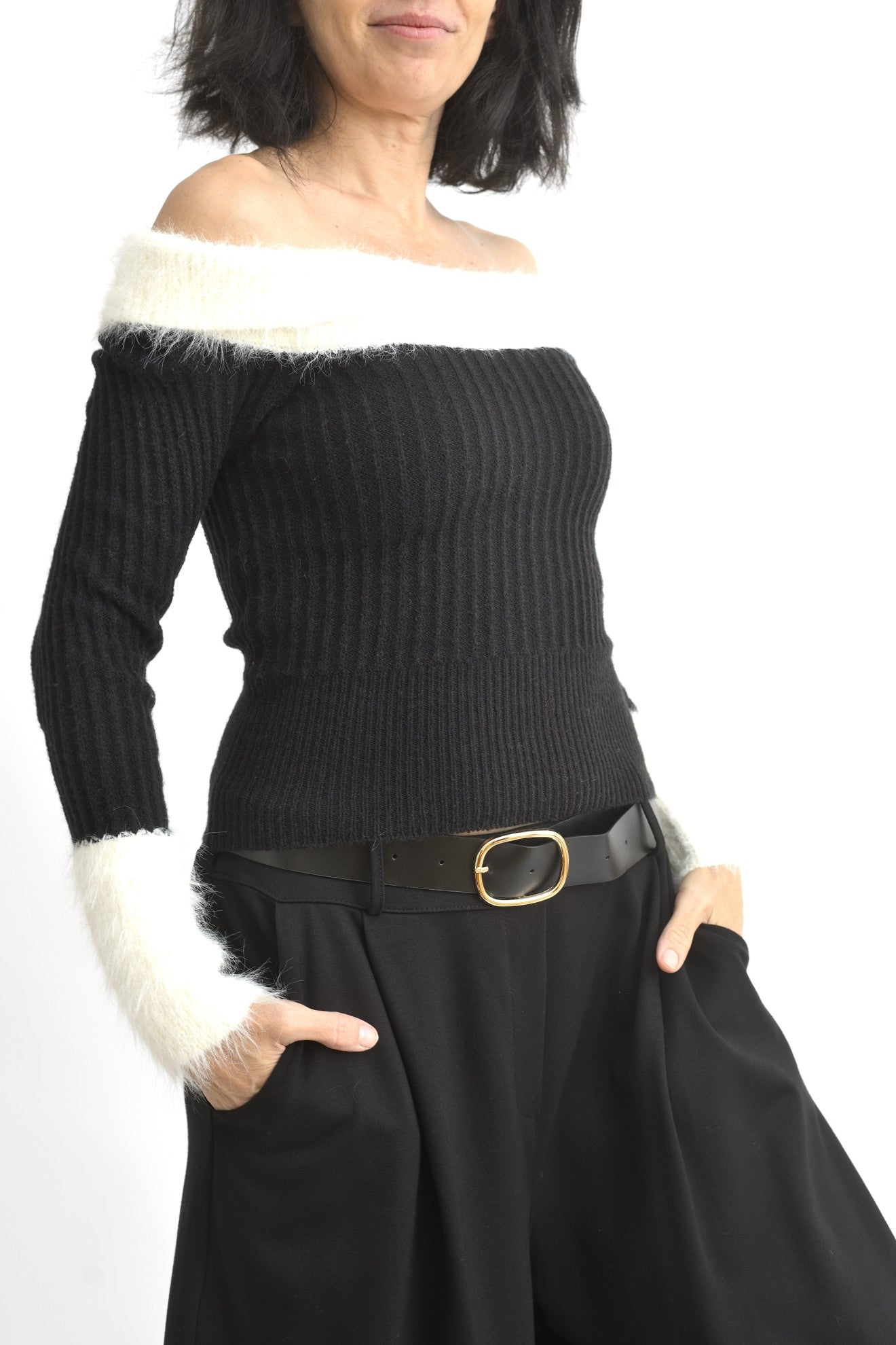 Vedere laterală a bluzei negre din tricot, cu umeri goi și mâneci lungi terminate cu manșete pufoase albe.