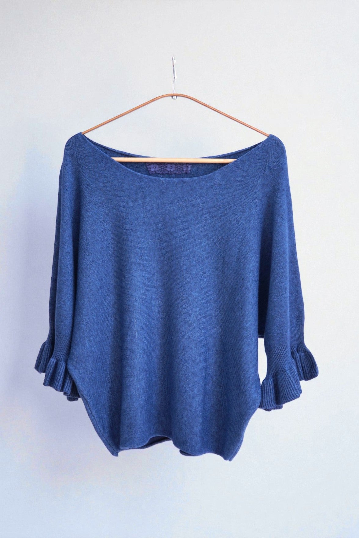 Detaliu textură moale a tricotului și finisaj volanat la mâneci, design elegant.