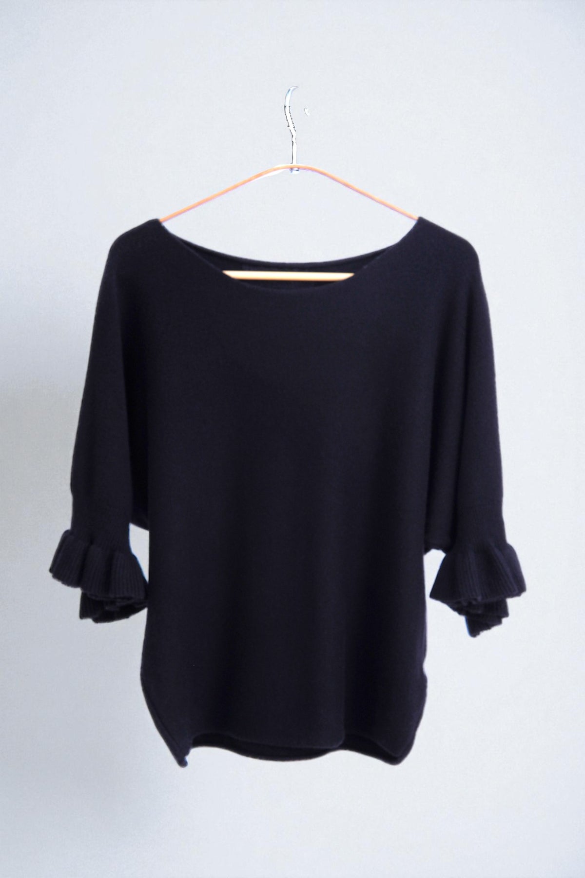 Detaliu textură moale a tricotului și finisaj volanat la mâneci, design elegant.