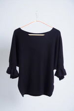 Detaliu textură moale a tricotului și finisaj volanat la mâneci, design elegant.