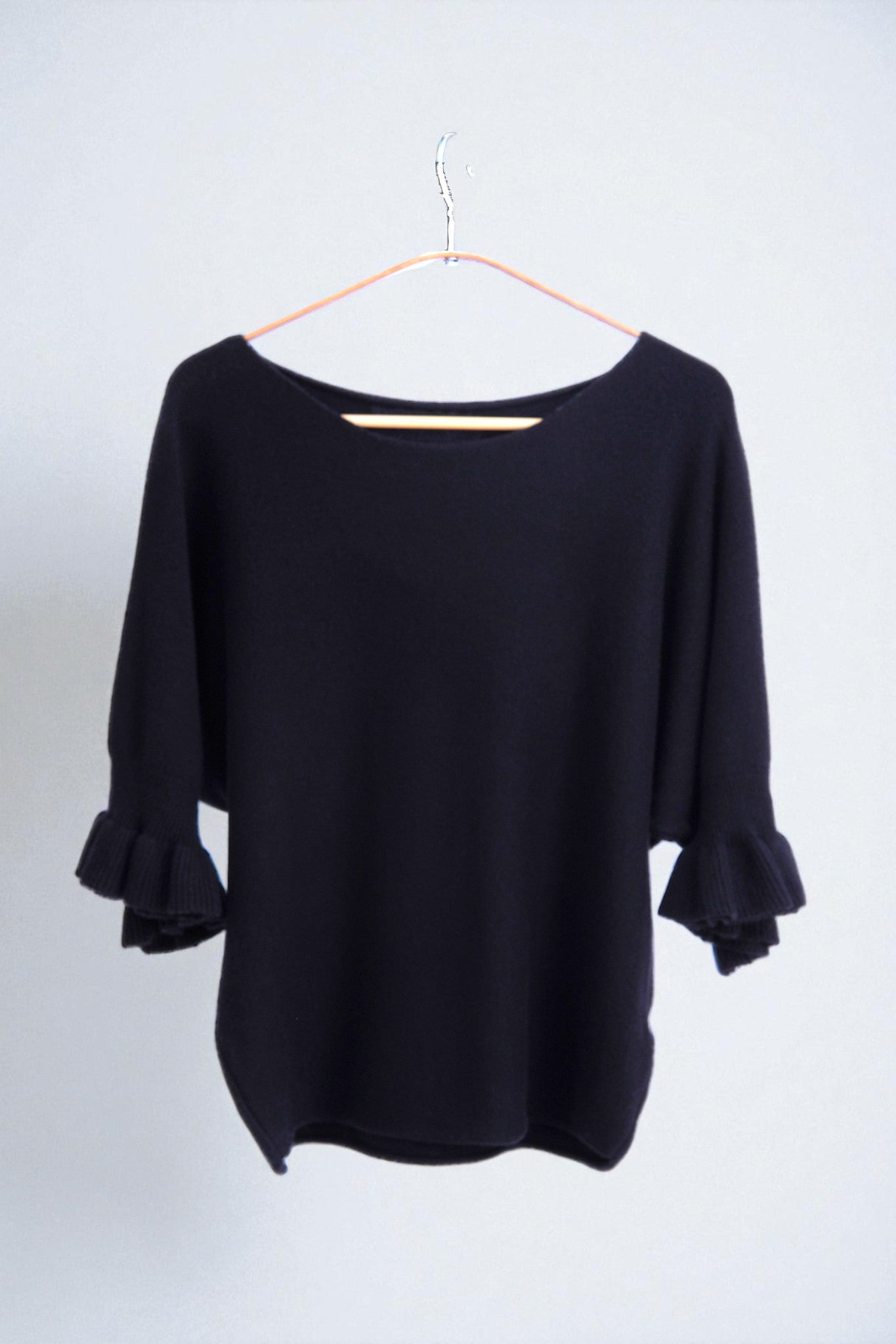 Detaliu textură moale a tricotului și finisaj volanat la mâneci, design elegant.