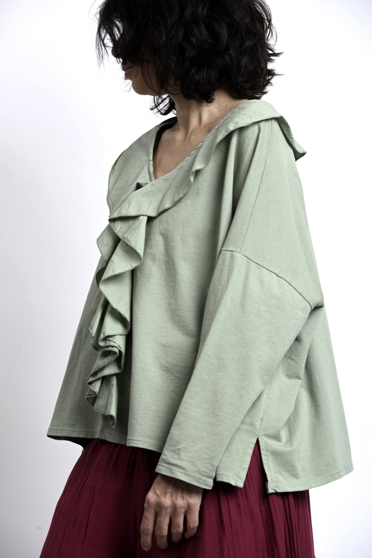 Prim-plan pe volanele frontale ale bluzei verde salvie, volum delicat și textură netedă, potrivită pentru layering.