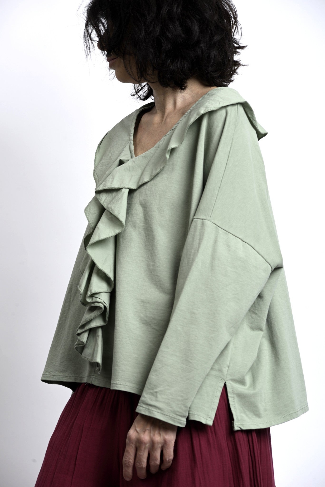 Prim-plan pe volanele frontale ale bluzei verde salvie, volum delicat și textură netedă, potrivită pentru layering.