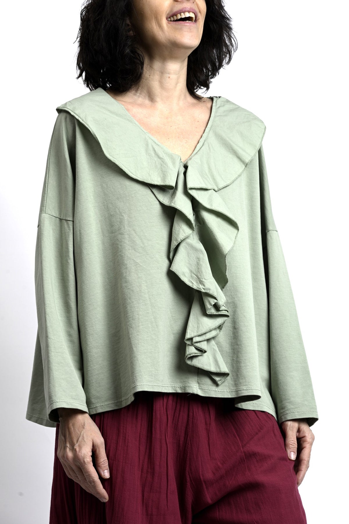 Vedere laterală bluză verde salvie cu mâneci lungi și croială oversize, umeri căzuți și cădere naturală.