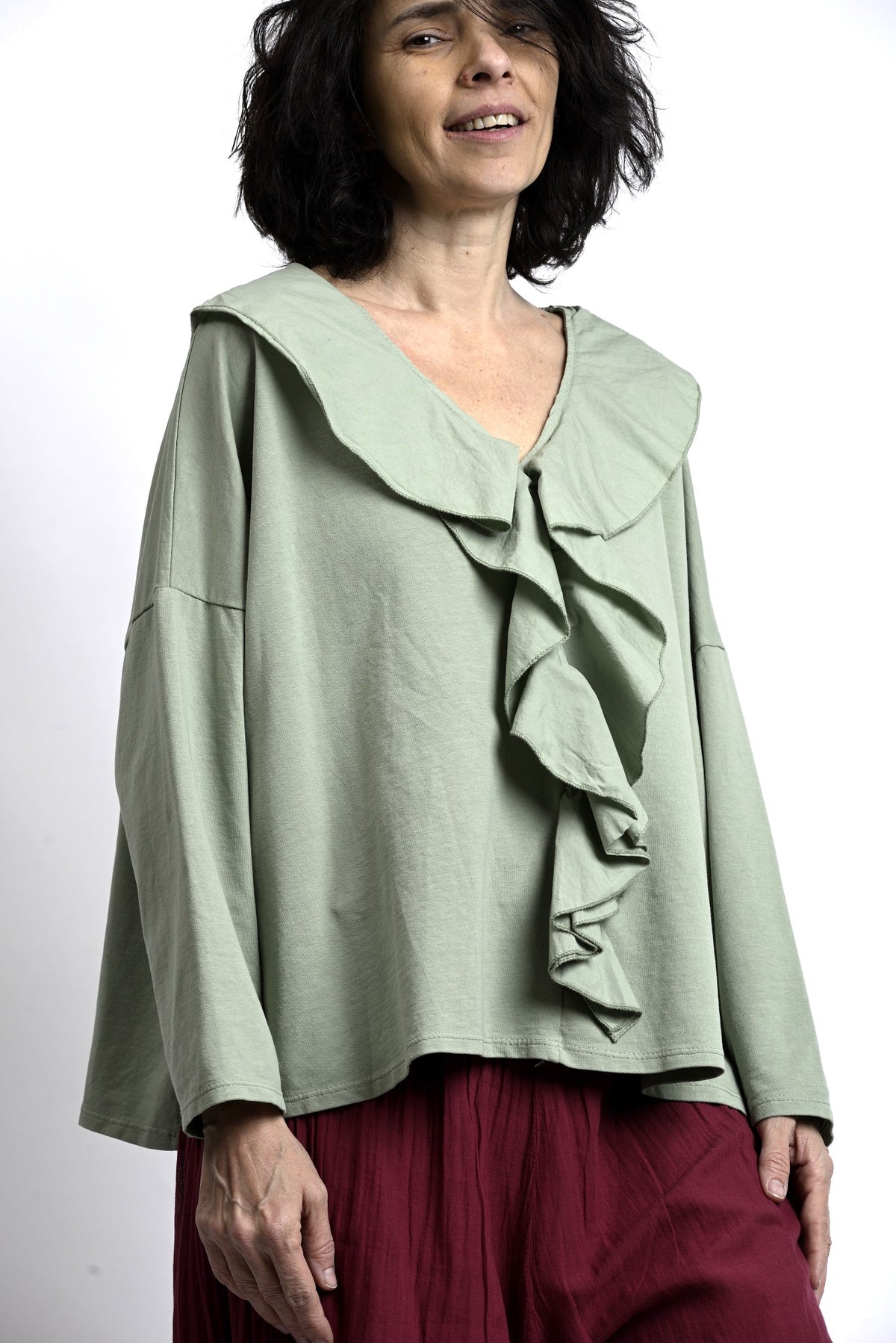 Bluză verde salvie cu volane frontale și guler amplu, croială lejeră cu umeri căzuți, vedere din față.