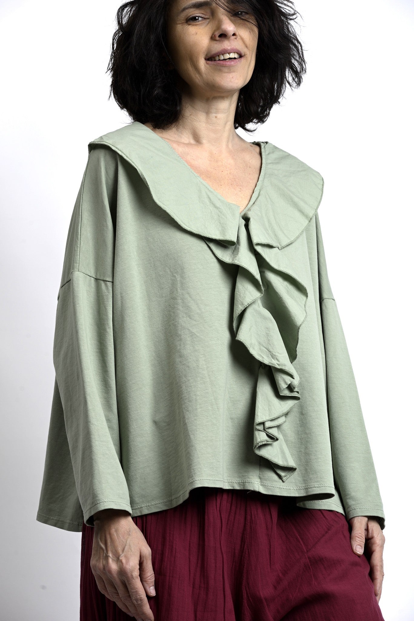 Bluză verde salvie cu volane frontale și guler amplu, croială lejeră cu umeri căzuți, vedere din față.