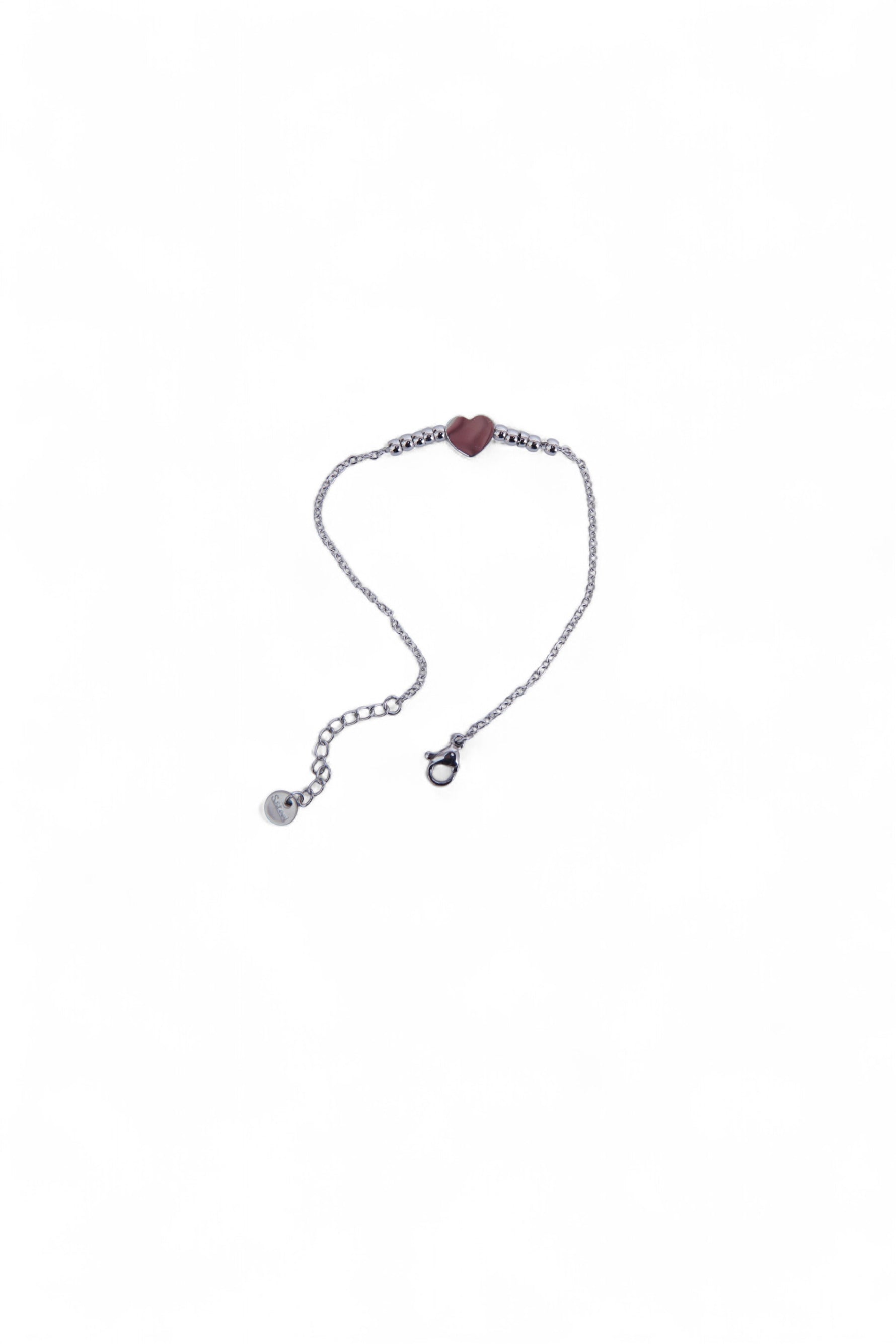 Brățară argintie din oțel inoxidabil, cu pandantiv inimă și biluțe mici, așezată delicat pe fundal alb.