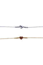 Două brățări subțiri din oțel inoxidabil, una argintie și una aurie, cu pandantiv inimă și biluțe decorative, fotografiate în detaliu pe fundal alb.