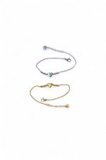 Două brățări din oțel inoxidabil, una argintie și una aurie, cu inimă centrală și lanț fin, așezate pe fundal alb, vedere de ansamblu.