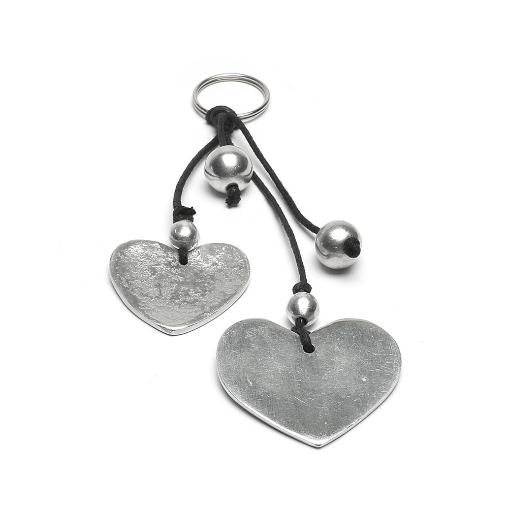 Breloc cu două inimioare din aluminiu reciclat și accesorii metalice pe șnur negru, prezentat pe fundal alb.
