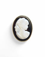 Broșă camee mare, ovală, cu un profil sculptat în alb pe un fundal negru, încadrată într-o ramă aurie elegantă.
